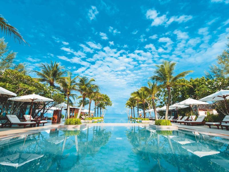 Ein großer Pool mit Palmen und Liegestühlen unter blauem Himmel und weißen Wolken.
