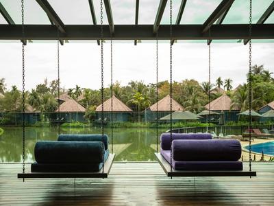 Moderní odpočinková zóna s houpacími křesly a výhledem na rybník a bungalovy v zeleni.