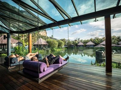 Zwei Personen entspannen auf einer Hängematte mit Blick auf einen Pool und Bungalows.