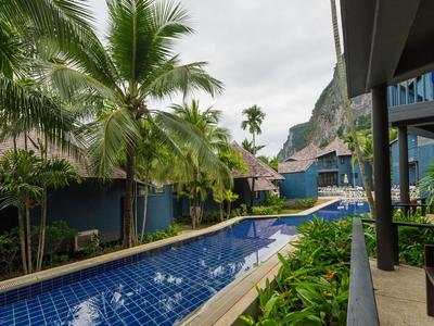 Jardin d'hôtel avec piscine, palmiers et chemin pavé sous un ciel nuageux