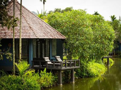 Bungalow sur pilotis au bord d'un lac calme avec végétation verte et chaises longues.