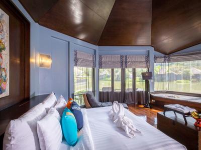 Moderní hotelový pokoj s velkou postelí, barevnými polštáři a výhledem na zelenou krajinu.