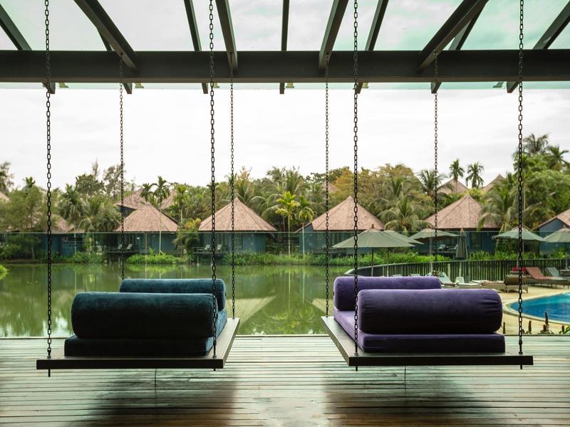 Moderní odpočinková zóna s houpacími křesly a výhledem na rybník a bungalovy v zeleni.