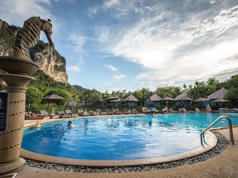 Kruhový hotelový bazén s lehátky a horskou krajinou v pozadí pod zataženou oblohou.