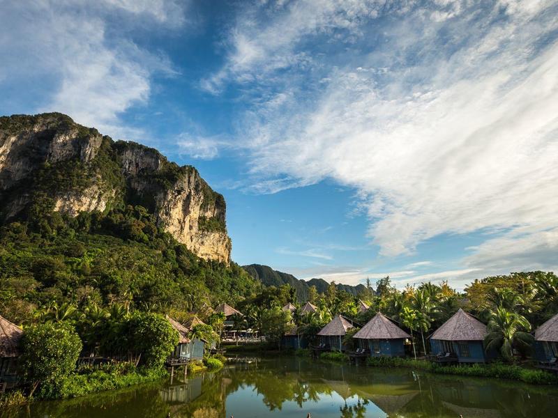Horská krajina s bungalovy u vody pod oblačnou oblohou.