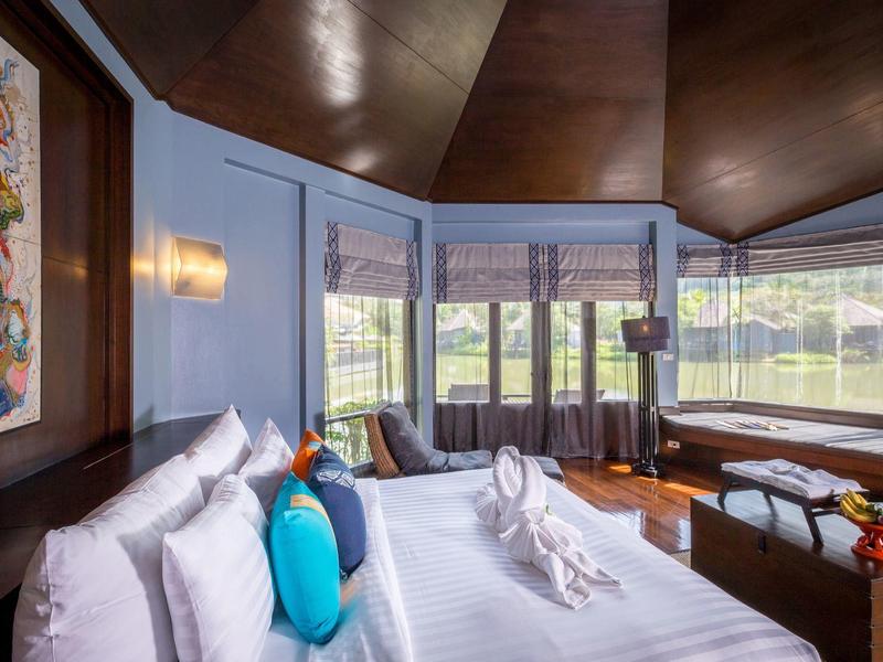 Moderní hotelový pokoj s velkou postelí, barevnými polštáři a výhledem na zelenou krajinu.