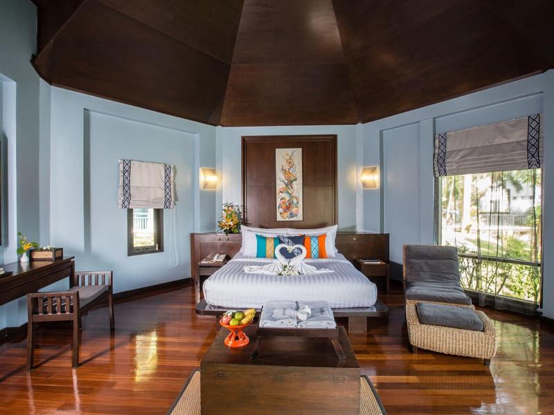 Elegantní hotelový pokoj s manželskou postelí, dřevěnou podlahou a velkými okny s výhledem do zeleně.