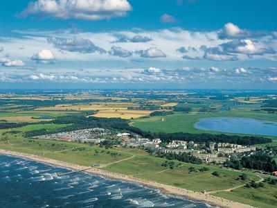 Küstenlandschaft mit Strand, Wellen, See, Feldern und blauen Himmel mit weißen Wolken.