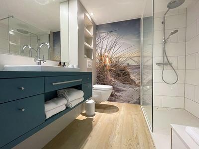 Modernes Badezimmer mit blauer Waschtischinsel, Dusche und Strandlandschaft als Wanddekoration.