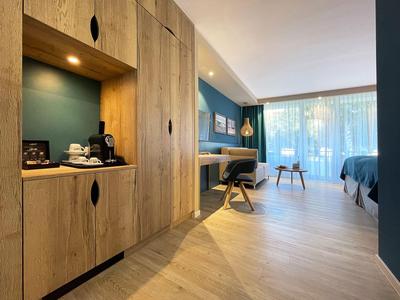 Modern eingerichtetes Hotelzimmer mit Holzschränken, Schreibtisch und großem Fenster mit Vorhängen.