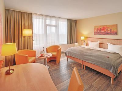Hell eingerichtetes Hotelzimmer mit Doppelbett, Sitzbereich und Schreibtisch.