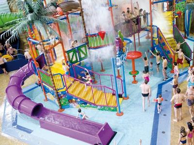 Buntes Indoor-Wasserspielplatz mit Rutschen, Klettergerüsten und palmengeschmücktem Bereich.