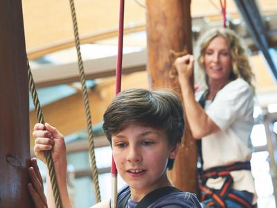 Ein Junge und eine Frau tragen Klettergurte und halten Seile im Innenbereich.