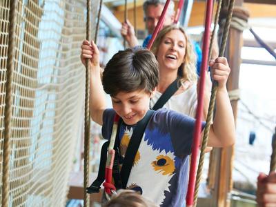 Kinder spielen fröhlich auf einem Klettergerüst aus Seilen und Holz in einem hellen Raum.