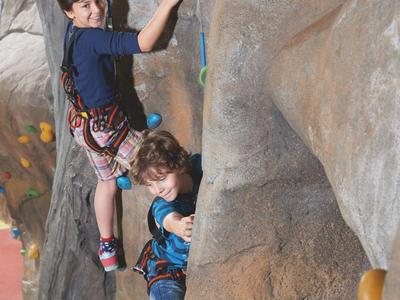 Two children climb an artificial rock wall inside an indoor climbing gym.