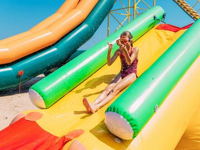 Child sliding joyfully on colorful water slide under sunny sky outdoors.