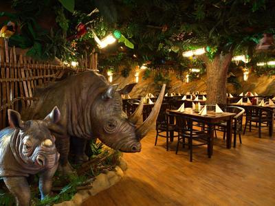 Restaurant mit Wildniskulisse, Holzboden, Bäumen und realistischen Nashornfiguren.