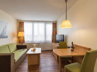 Lichte woonkamer met groene bank, houten meubels en raam met doorschijnende gordijnen.