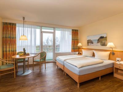 Lichte hotelkamer met twee bedden, tafel met stoelen en balkonuitzicht.