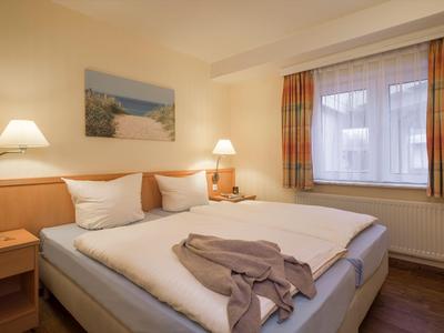Licht hotelkamer met tweepersoonsbed, leeslampen en raam met gordijnen.
