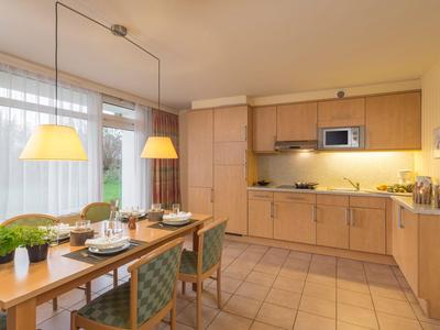 Lichte eetkamer met houten meubels, groene stoelen en grote ramen in hotelkamer.