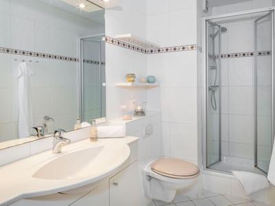 Moderne badkamer met toilet, douche, grote spiegel en witte inrichting.