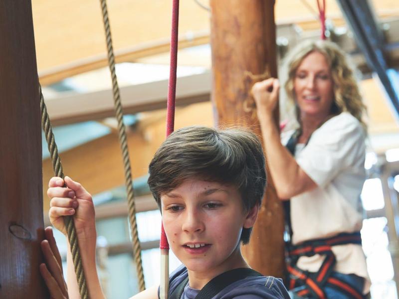Ein Junge und eine Frau tragen Klettergurte und halten Seile im Innenbereich.