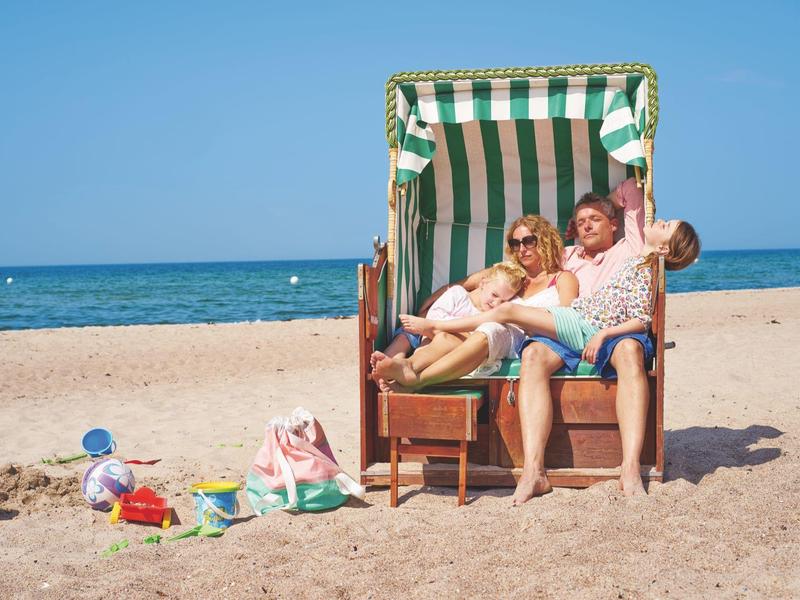 Älteres Ehepaar sitzt im gestreiften Strandkorb am Sandstrand mit Meer im Hintergrund bei Sonnenschein.