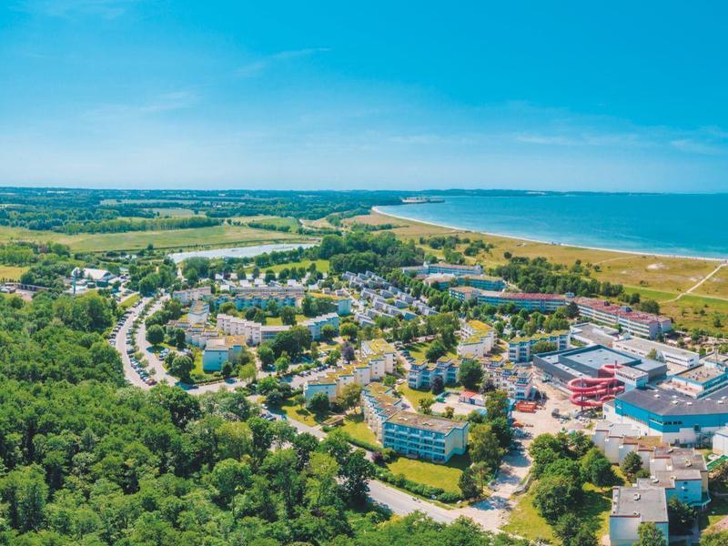 Luftaufnahme einer Küstenstadt mit grünen Wäldern, Gebäuden und blauem Meer im Hintergrund.