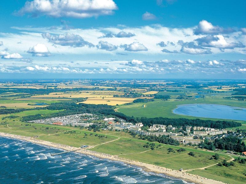 Küste mit Sandstrand, grünen Feldern, Dorf und See unter blauem Himmel mit Wolken.
