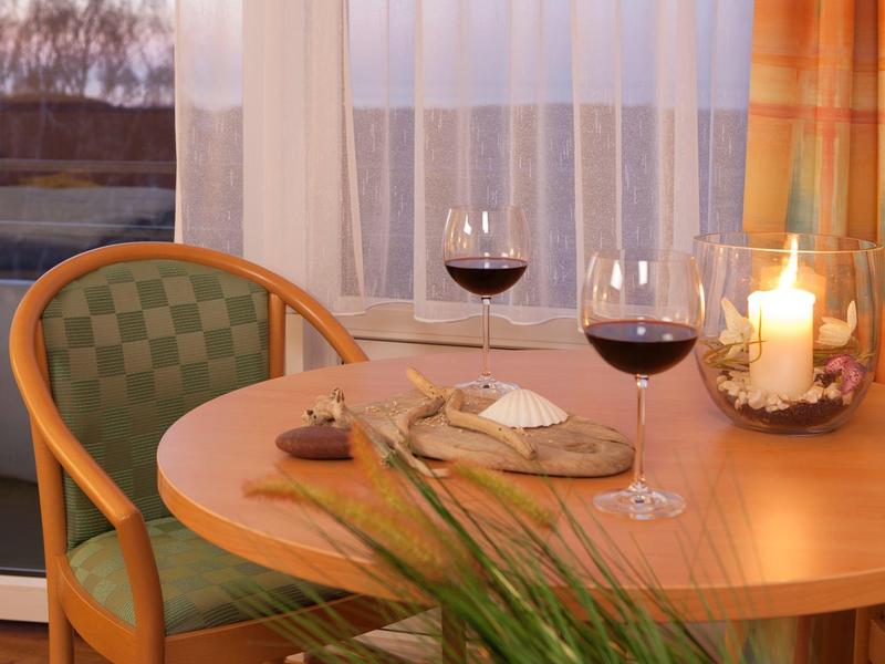 Runder Holztisch mit zwei gefüllten Weingläsern, Kerze und Käsebrett vor Fenster mit Vorhängen.