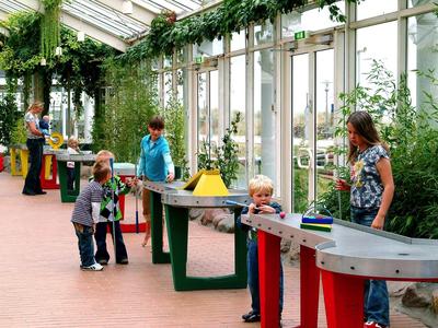 Kinder spielen an interaktiven Tischen in einem hellen, begrünten Raum mit großen Fenstern.
