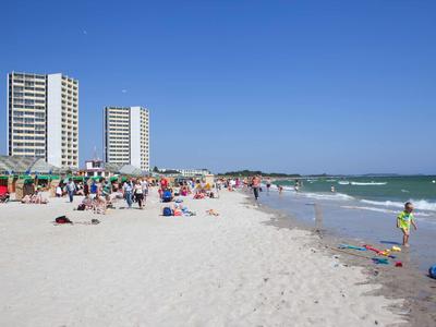 Breiter Sandstrand mit Menschen, Hochhäusern und klarem blauem Himmel am Meer.