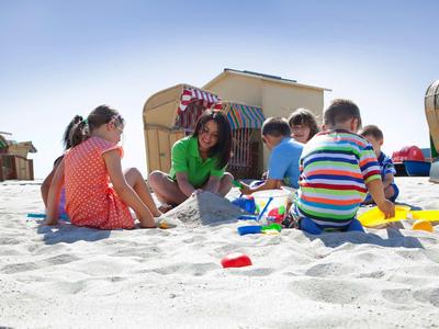 Kinder spielen im Sand an einem sonnigen Strand mit Strandkörben im Hintergrund.