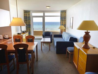 Helles Hotelzimmer mit Meerblick, Sitzbereich und Esstisch mit vier Stühlen.