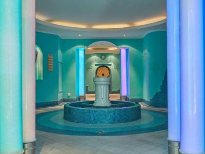 Modernes Spa mit zentralem Wasserspender und farbigen, beleuchteten Säulen in kühlem Blau- und Grünton.