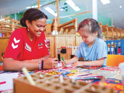 Frau und Kind malen gemeinsam an einem Tisch mit bunten Stiften in einer kinderfreundlichen Umgebung.