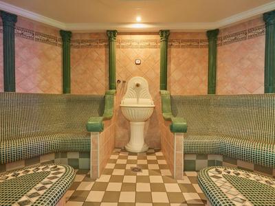 Traditioneller Spa-Raum mit Mosaikbänken und zentraler Bodenbrunnenanlage.