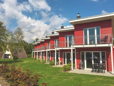 Rote Ferienhäuser mit Balkonen neben gepflegtem Rasen und Tepee-Zelten unter blauem Himmel.