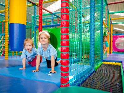 Zwei Mädchen spielen in einem bunten Indoor-Spielplatz mit Klettergerüsten und Trampolin.