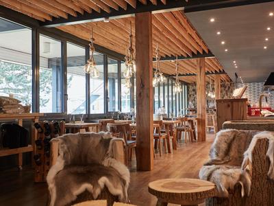 Gemütlicher Hotel-Loungebereich mit Holzmöbeln, Fellauflagen und großen Fenstern.