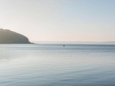 Weites, ruhiges Meer mit sanften Wellen, weiter Horizont und bewaldeter Hügel links im Bild.