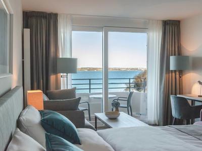 Helles Schlafzimmer mit Doppelbett, Sitzbereich, Schreibtisch und Balkon mit Meerblick.