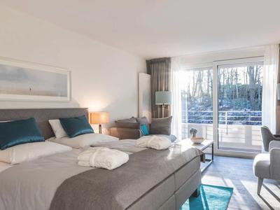 Helles Schlafzimmer mit Doppelbett, Sitzecke, großem Fenster und Blick ins Grüne.