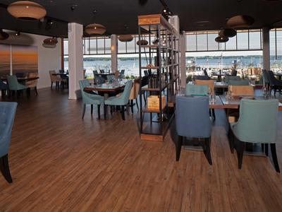 Moderner Speiseraum mit Stühlen und Tischen, großer Fensterfront mit Blick auf Wasser und Stadt.