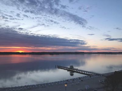 Sonnenuntergang über einem ruhigen See mit einem langen Steg im Vordergrund.