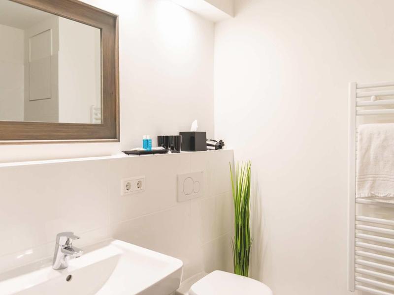 Helles, modernes Badezimmer mit weißem Waschbecken, großem Spiegel und Handtuchheizung.