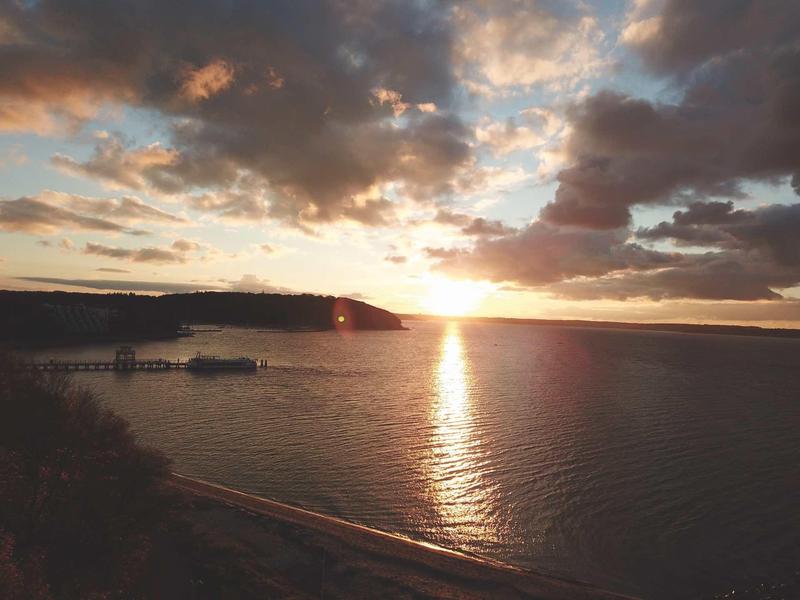 Sonnenuntergang über einem ruhigen See mit bewölktem Himmel und einem Steg am Ufer.