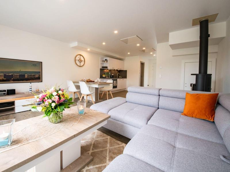 Bright living room with gray corner sofa, orange pillow, modern furniture, and open kitchen.