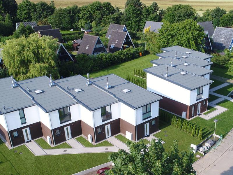 Several modern white vacation houses with dark accents in a green rural setting.
